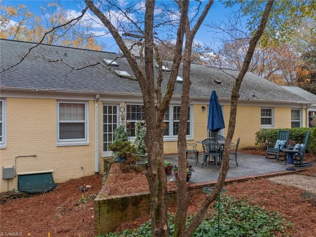 back of property with a patio, brick siding, and roof with shingles