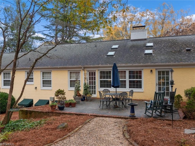 rear view of property with a patio area, brick siding, roof with shingles, and a chimney