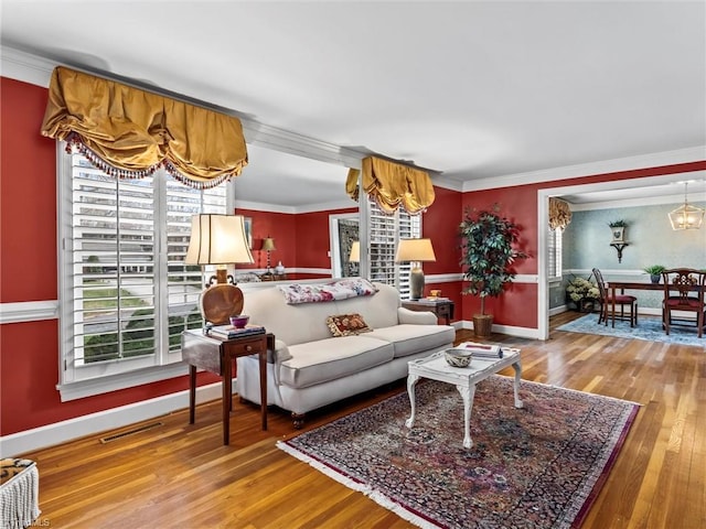 living room with crown molding, wood finished floors, visible vents, and baseboards