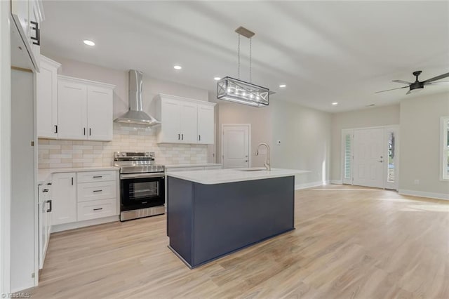 kitchen with white cabinetry, stainless steel electric range oven, wall chimney exhaust hood, and an island with sink