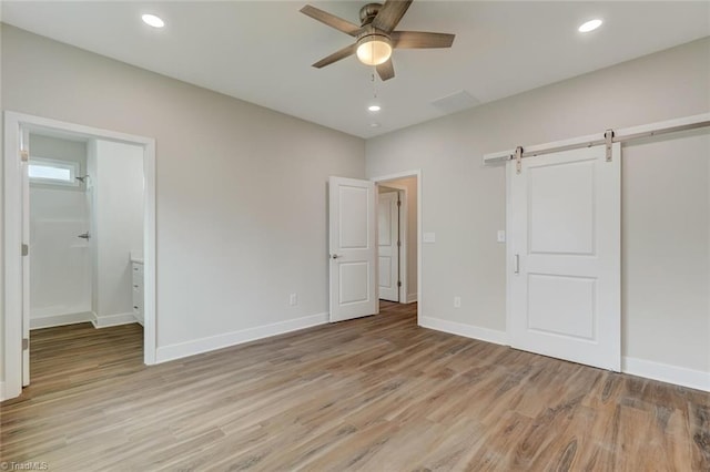 unfurnished bedroom with ceiling fan, a barn door, light wood-type flooring, and ensuite bathroom