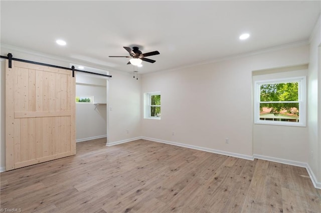 unfurnished bedroom with a barn door, wood finished floors, and crown molding