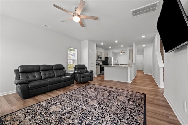 living area featuring baseboards, a ceiling fan, light wood-style flooring, and visible vents