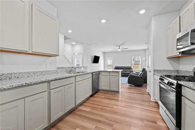 kitchen with a ceiling fan, a sink, a peninsula, open floor plan, and stainless steel appliances