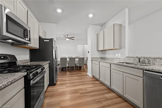 kitchen featuring light stone countertops, light wood-style floors, ceiling fan, a sink, and stainless steel appliances