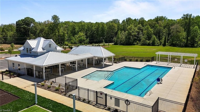 pool featuring a lawn, a patio area, fence, a wooded view, and a pergola