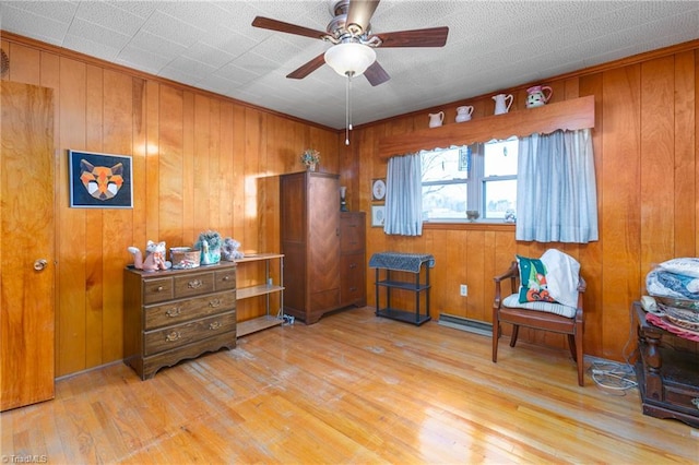 sitting room featuring wood walls, ceiling fan, light hardwood / wood-style floors, and a baseboard heating unit