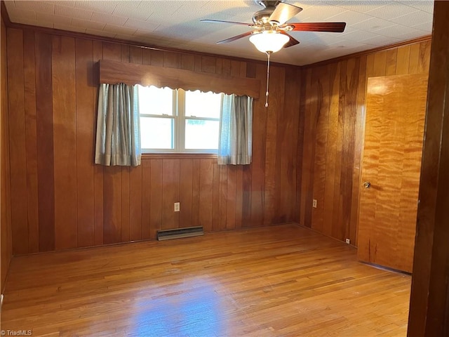 unfurnished room with light hardwood / wood-style flooring, ceiling fan, wood walls, and a baseboard radiator