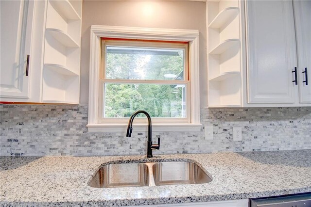 kitchen with white cabinetry, sink, light stone counters, and tasteful backsplash