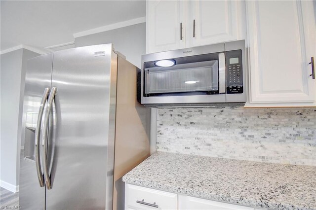 kitchen with light stone countertops, stainless steel appliances, tasteful backsplash, and white cabinetry