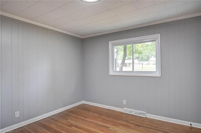 unfurnished room with wood-type flooring, wooden walls, and ornamental molding