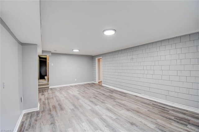 basement with light hardwood / wood-style floors and brick wall