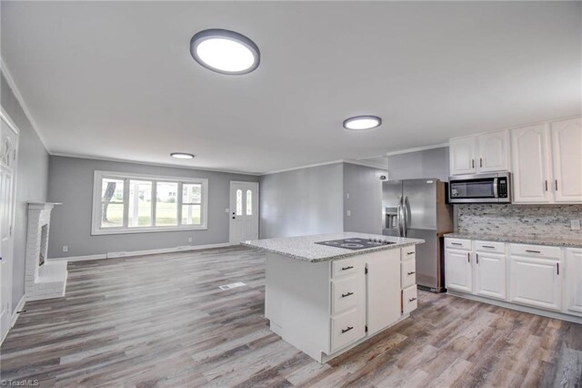 kitchen with appliances with stainless steel finishes, light wood-type flooring, a kitchen island, and white cabinets