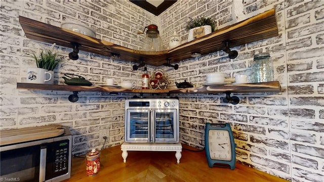 bar with wine cooler, brick wall, and hardwood / wood-style flooring