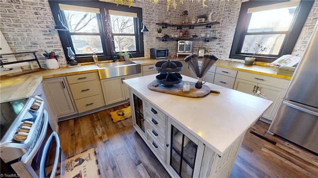 kitchen featuring stainless steel appliances, a kitchen island, brick wall, and dark wood-type flooring