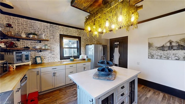 kitchen featuring stainless steel appliances, a center island, brick wall, dark wood-type flooring, and white cabinetry