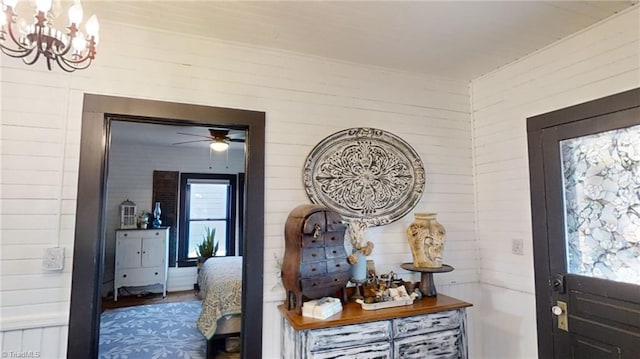 foyer with ceiling fan with notable chandelier and wood walls