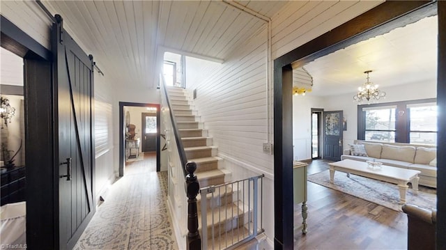 hall with hardwood / wood-style floors, wooden ceiling, wood walls, a barn door, and a chandelier