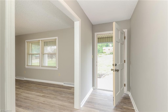 foyer entrance with a baseboard radiator, a textured ceiling, baseboards, and light wood-style floors