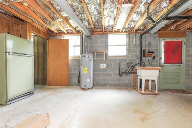 below grade area featuring freestanding refrigerator, concrete block wall, and water heater