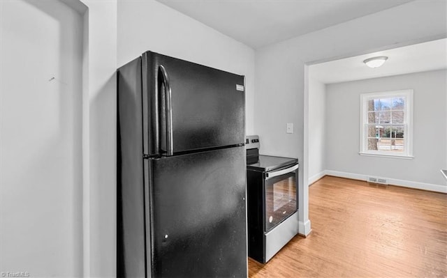 kitchen with black refrigerator, stainless steel electric range, and light wood-type flooring