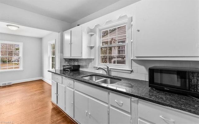 kitchen with sink, tasteful backsplash, wood-type flooring, dark stone countertops, and white cabinets