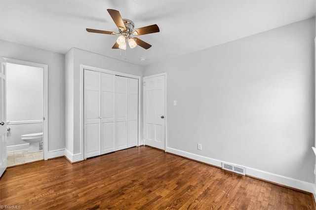 unfurnished bedroom with wood-type flooring, ensuite bathroom, ceiling fan, and a closet