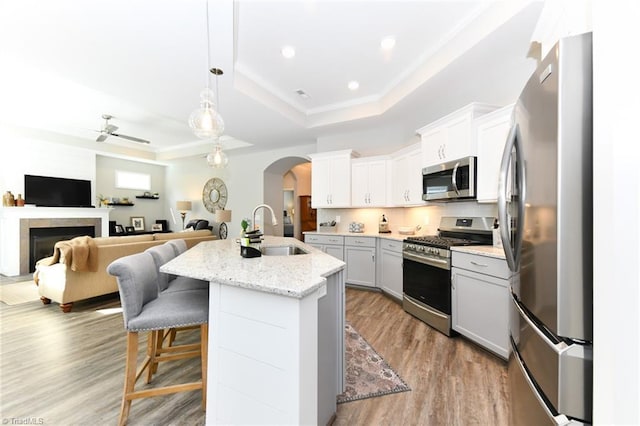 kitchen featuring ceiling fan, appliances with stainless steel finishes, arched walkways, a sink, and a raised ceiling