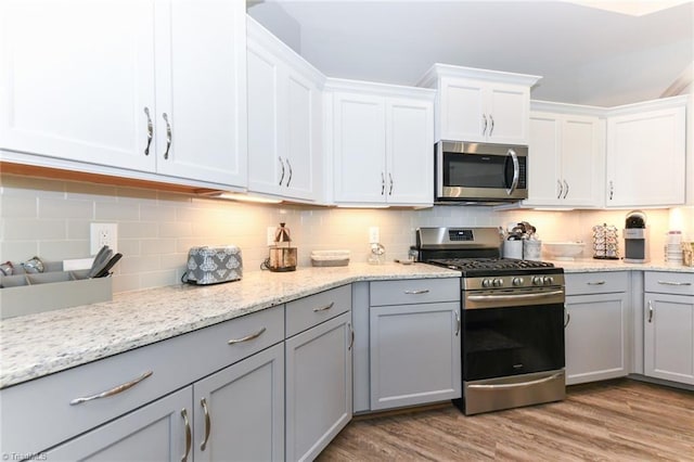 kitchen with white cabinets, tasteful backsplash, light wood-style flooring, gray cabinetry, and stainless steel appliances