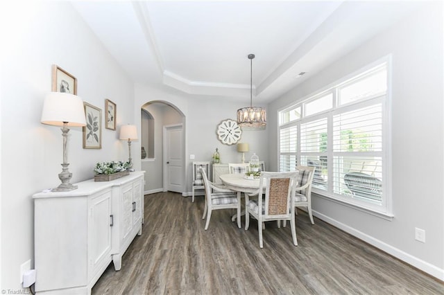 dining room with a raised ceiling, arched walkways, a chandelier, baseboards, and wood finished floors