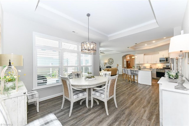 dining space with arched walkways, dark wood-style floors, an inviting chandelier, ornamental molding, and a tray ceiling