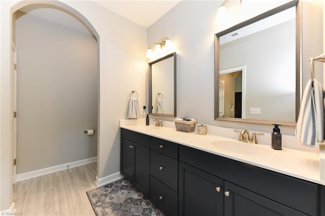 full bathroom featuring a sink, baseboards, double vanity, and wood finished floors