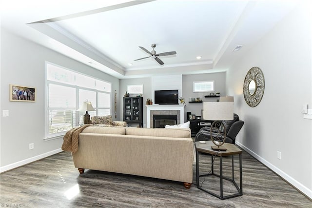 living room featuring a raised ceiling, a fireplace, a ceiling fan, and dark wood-style flooring