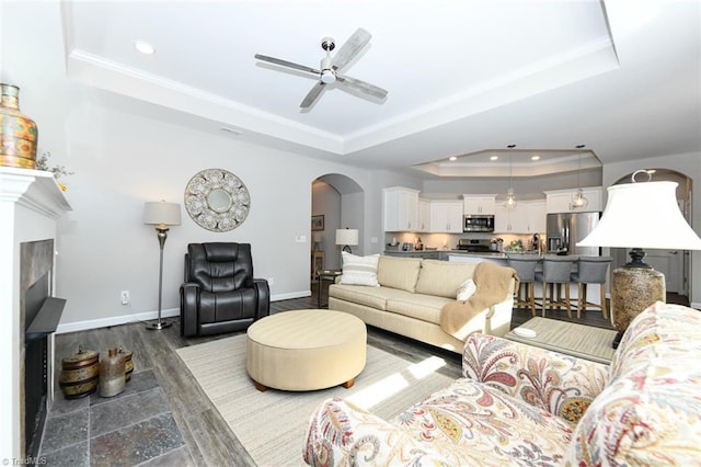 living area featuring recessed lighting, a ceiling fan, arched walkways, and a tray ceiling