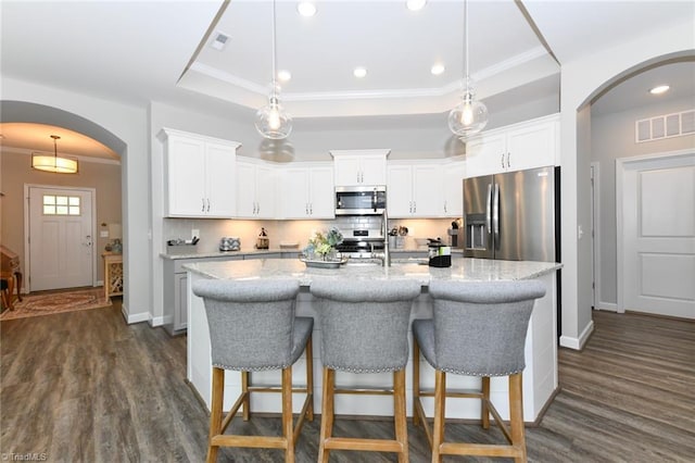 kitchen with appliances with stainless steel finishes, a tray ceiling, arched walkways, and dark wood-style floors