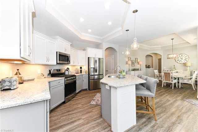 kitchen with light wood finished floors, arched walkways, stainless steel appliances, a kitchen bar, and a tray ceiling