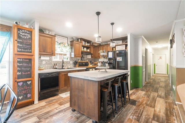 kitchen featuring decorative light fixtures, sink, a kitchen breakfast bar, a center island, and black appliances