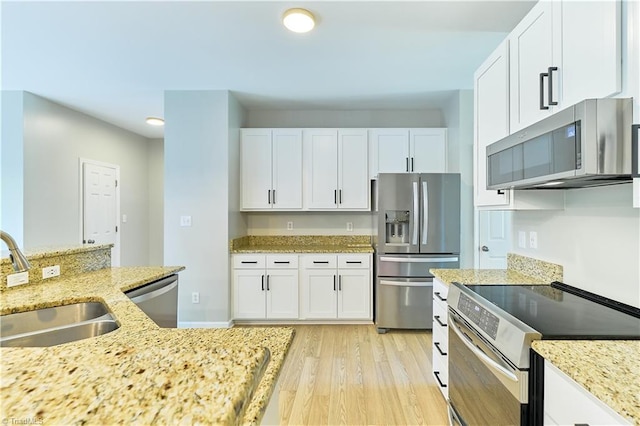 kitchen with white cabinets, light stone countertops, a sink, light wood-style flooring, and stainless steel appliances