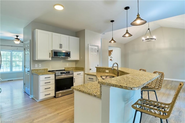 kitchen featuring ceiling fan, appliances with stainless steel finishes, a sink, a breakfast bar area, and light wood-type flooring
