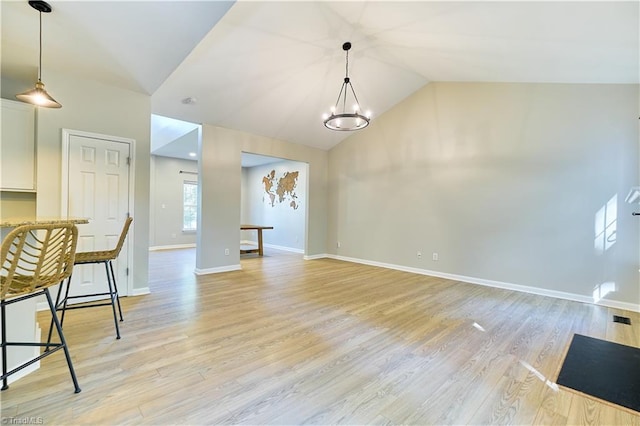 unfurnished dining area featuring baseboards, a chandelier, light wood-style flooring, and lofted ceiling