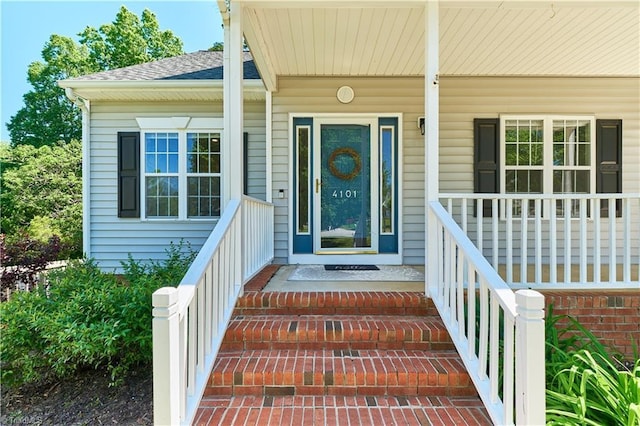 view of exterior entry with a shingled roof and a porch