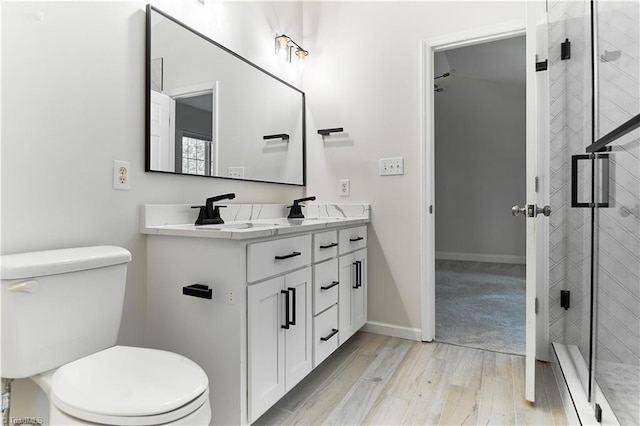 full bath with double vanity, toilet, baseboards, wood finished floors, and a stall shower