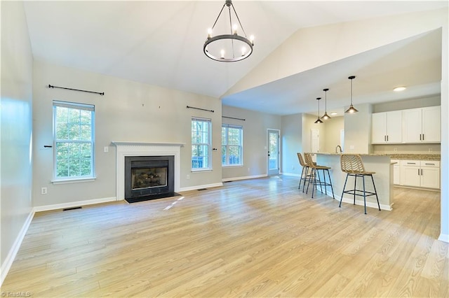 living area with high vaulted ceiling, baseboards, light wood finished floors, and a chandelier