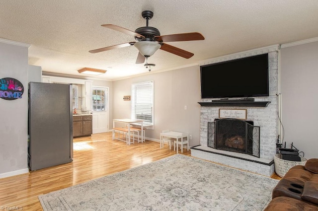 living room with ceiling fan, a textured ceiling, light wood-type flooring, and ornamental molding