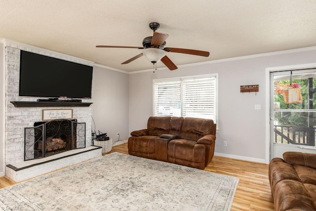 living room featuring ceiling fan, a textured ceiling, hardwood / wood-style floors, a fireplace, and crown molding