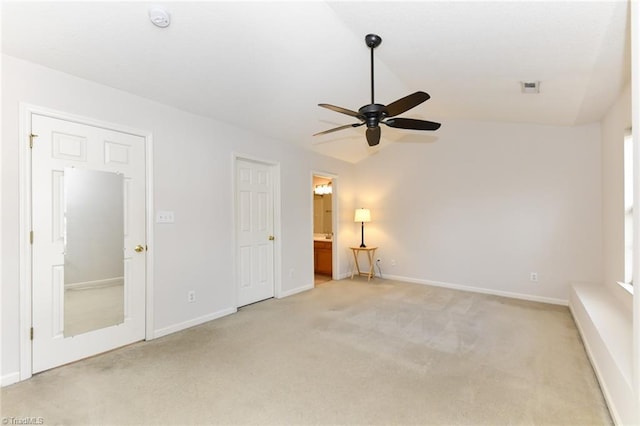 interior space featuring lofted ceiling, light colored carpet, ensuite bath, and baseboards