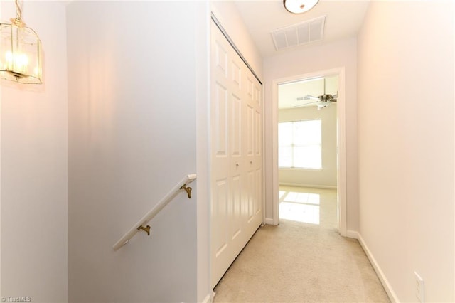 hall featuring baseboards, visible vents, light carpet, and an upstairs landing