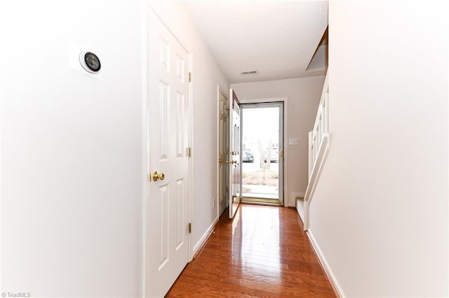 corridor featuring visible vents, a textured ceiling, baseboards, and wood finished floors