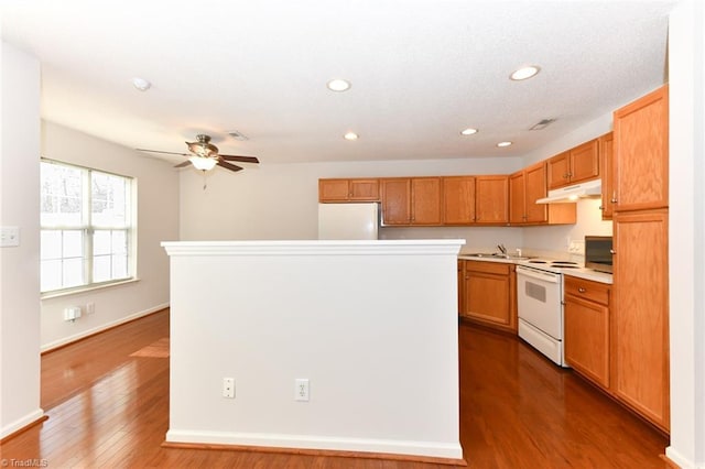 kitchen featuring white appliances, a kitchen island, wood finished floors, light countertops, and under cabinet range hood