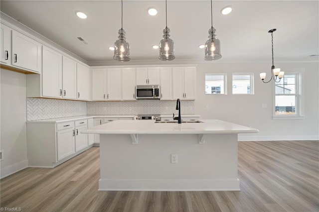 kitchen with hanging light fixtures, white cabinets, and an island with sink